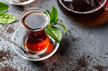 Glass cup of black tea with fresh tea leaves, traditional turkish brewed hot drink
