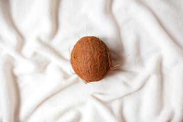 One whole coconut lies on a white soft cloth.