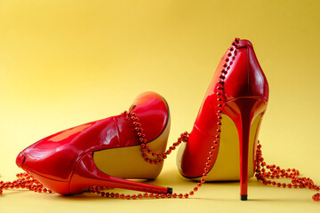 patent leather shiny female red stilettos and beads on a yellow background