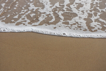 Soft waves of the blue ocean on the sandy beach, aqua Foam bubbles, summer Holiday Background.