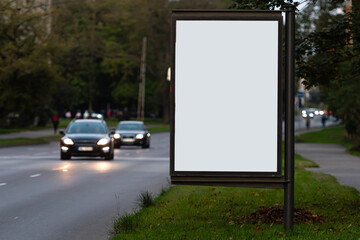 vertical blank billboard on the city street, in the background the blurred evening street with cars