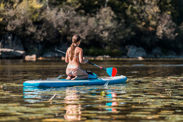 Young athletic  woman in bikini SUP stand up paddle board on a river overgrown with grass in Montenegro
