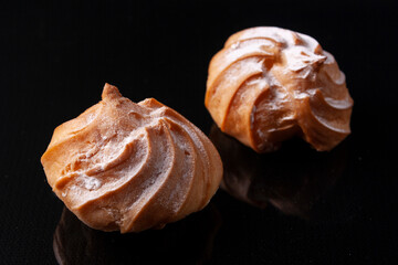 Custard profiteroles with custard on a black mirrored background.