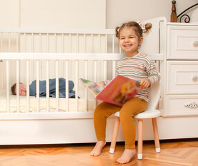 Cute portrait of toddler sister with  baby brother. Little girl playing with her newborn brother. Big sister meet her infant brother first time after his born. Family with 2 children. Real people.