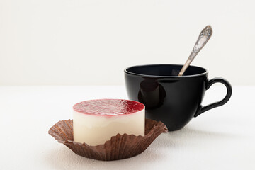 Tea in a black mug with a spoon, with a cake on a light background