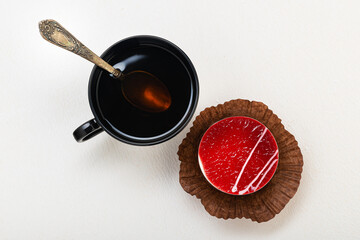 Tea in a black mug with a spoon, with a cake on a light background