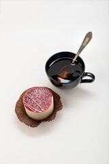 Tea in a black mug with a spoon, with a cake on a light background
