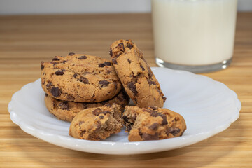 Chocolate chip cookies with glass of milk in the background, on a wooden table.