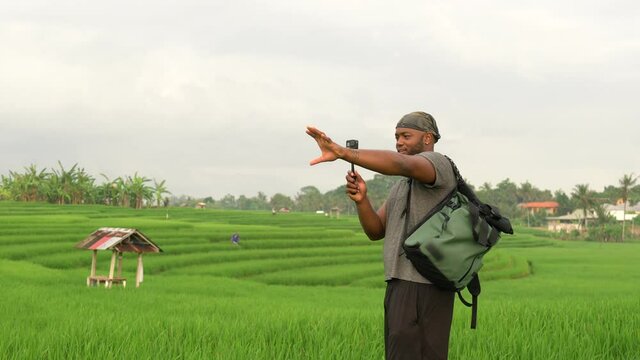 African American male blogger with monopod and go pro camera shooting influence travel vlog during summer vacations for visiting Indonesia, millennial tourist talking on selfie video