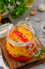 Roasted marinated bell pepper with garlic and spices in a jar on a board on a gray concrete background. Copy space.