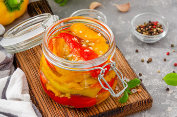 Roasted marinated bell pepper with garlic and spices in a jar on a board on a gray concrete background. Copy space.