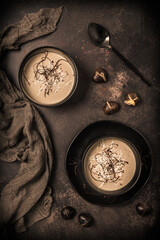 Two black bowls of chestnut soup with parmesan, chilli flakes and threads on dark brown background, top view