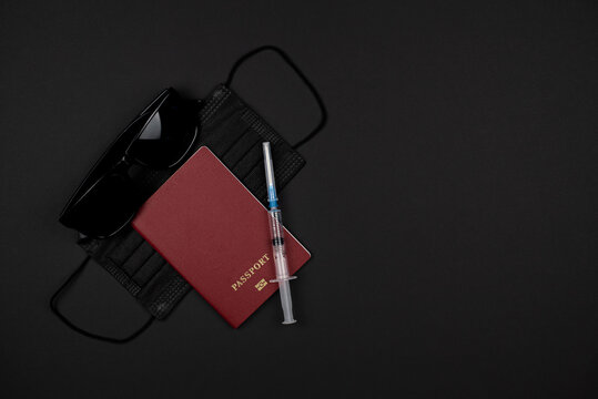 On a black background, a passport, black glasses, a black medical mask and a syringe. Quarantine travel concept