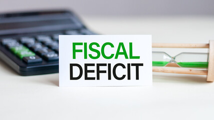 Business concept. Notebook with text FISCAL DEFICIT sheet of white paper for notes, calculator, hourglass in the white background