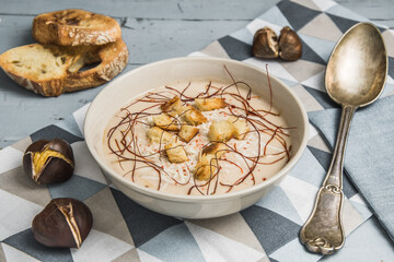 Chestnut soup with parmesan, croutons and chilli flakes and threads on grey wooden background, decorated with roasted bread and chestnuts