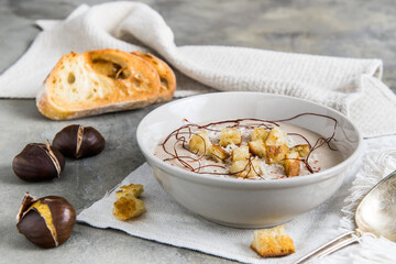 Chestnut soup with parmesan, croutons and chilli flakes and threads on grey concrete background, decorated with roasted bread and chestnuts