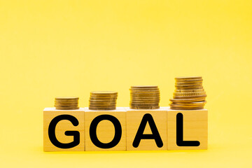 wooden cubes with GOAL word and stcack of coins . Business success goal concept.