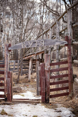 Old fence for animals in a forest reserve. At the entrance to the pen, the name of the animal in Russian is Kuzya. An empty corral with an open gate.