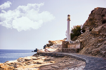 Crete, Greece - Wide angle shot of a rocky path against a white light house situated on a hill in a center of island