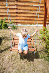 Kid toddler boy swinging on a playground swing in the backyard at summer