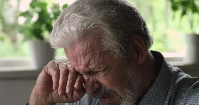 Close up head shot depressed elderly mature hoary man crying, feeling desperate, mourning alone at home, having psychological problems. Dementia alzheimer mental senile disease, loneliness concept.