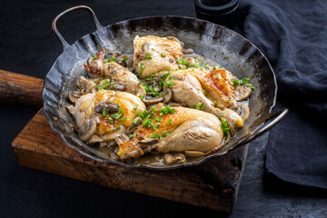 Traditional fried chicken wings and legs with mushrooms in wine sauce served as close-up in a rustic wrought iron frying pan