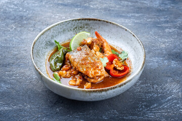 Modern style traditional Mexican seafood pozole soup with fish, king prawns and hominy in a clear sauce served as close-up in design bowl