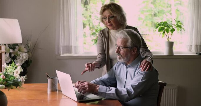 Happy bonding old middle aged caucasian family couple looking at computer screen, choosing buying goods in internet store, discussing online purchases, elderly generations and modern tech concept.