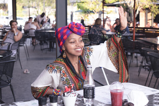 Fashionable African lady wearing a doek or head scarf waving at a friend