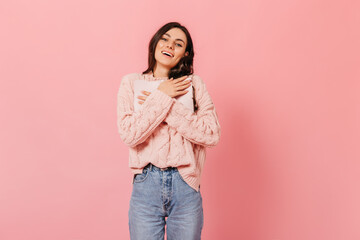Portrait of girl in pink sweater and mom jeans on isolated background. Blue-eyed brunette with dimpled cheeks presses important diary to her chest