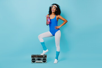 Attractive african lady in aerobics outfit standing on boombox. Studio shot of wonderful black girl...