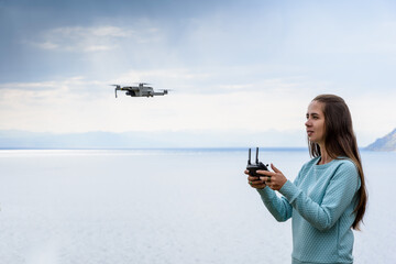 Beautiful young woman having fun with a mini drone outdoors. The girl stands against water background - Powered by Adobe