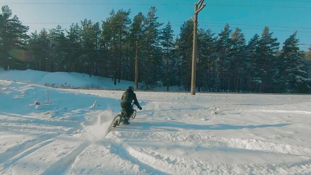 Cyclist in Black Clothes, Helmet and Snow Glasses Riding on Electric Bike in the Snow in Winter Forest. E-Bike Riding and Drifting at Cold Sunny Day - Super Slow Motion