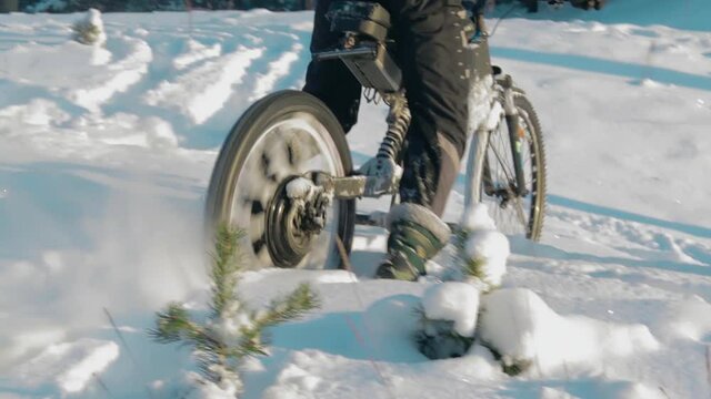 Cyclist in Black Clothes, Helmet and Snow Glasses Riding on Electric Bike in the Snow in Winter Forest. E-Bike Riding and Drifting at Cold Sunny Day - Slow Motion