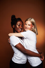 two pretty girls african and caucasian blond posing cheerful together on brown background, etnithity diverse lifestyle people concept