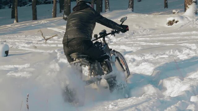 Cyclist in Black Clothes, Helmet and Snow Glasses Riding on Electric Bike in the Snow in Winter Forest. E-Bike Riding and Drifting at Cold Sunny Day - Slow Motion