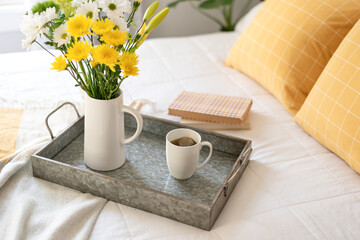 Cup of hot tea and flowers on a tray in the bedroom