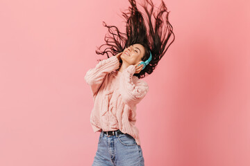 Lady in great mood is listening to song and playing with hair. Brunette with headphones laughs on pink background