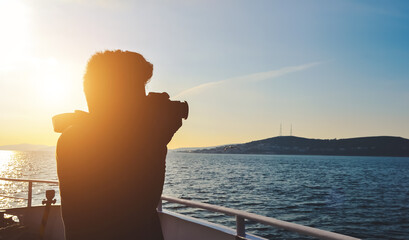 Silhouette of a young man taking a photo of water landscape with DSLR camera from a boat in the morning. Concept of success, hobby, photography, and entrepreneurship, also good for copy space