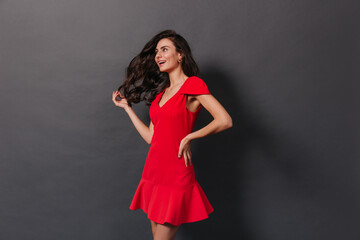 Beautiful woman with magnificent wavy hair posing in red outfit on dark background