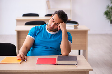 Exhausted male student preparing for the exams in the classroom