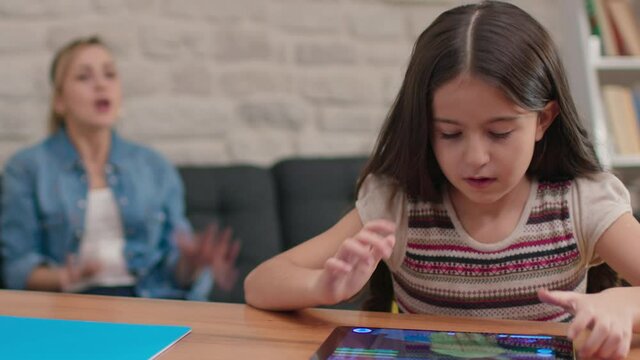 The mother yells at her daughter who does not do her homework and is constantly playing games on the tablet computer, the little girl covers her ears with her fingers.