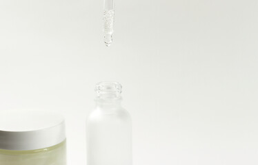 White transparent cosmetic bottle and pipette with drop of oil serum liquid essence on white background, cosmetics laboratory, dropper and hygiene 