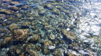 Transparent ocean water shining in the sun. Pebble bottom below crystal clear water.       