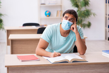 Young male student sitting in the classroom wearing mask