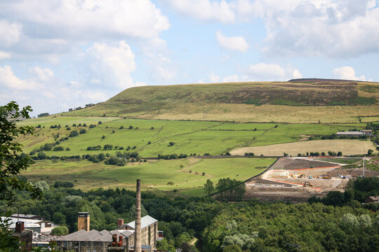 Mossley, England - A green hill and valley with a mill in front of them on the outskirts of Mossley on a summer day.  Image has copy space.