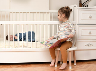 Cute portrait of toddler sister with  baby brother. Little girl playing with her newborn brother. Big sister meet her infant brother first time after his born. Family with 2 children. Real people.