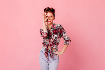 Gorgeous woman in jeans showing okay sign. Laughing pinup girl gesturing on pink background.