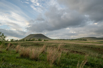 Fototapeta premium Hilly area covered with green grass. Solitary mountain, very beautiful, cloudy sky. There is free space for insertion.