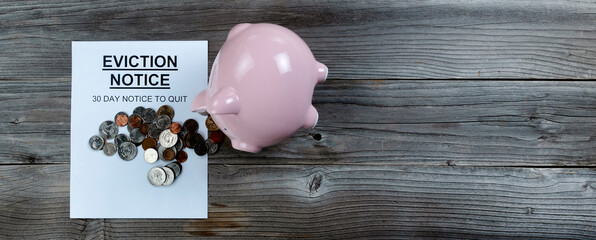 Eviction notice with toppled piggy bank spilling change on rustic wooden table in flat lay format